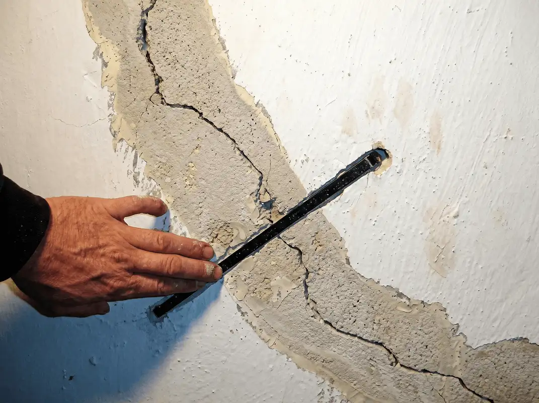A wall with a large crack is being inspected by a professional in Tulsa, OK